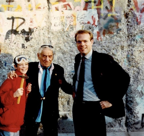 Young boy with a red coat and goggles holding a hammer and chisel, with Leonard Bernstein and his assistant Craig Urquhart at the Berlin Wall, 1989.
