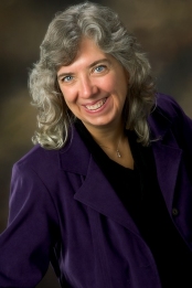 Photo of a white woman with long wavy grey hair wearing a dark purple blouse.