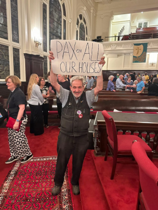 Man holding up a sign reading Pax On All Our Houses