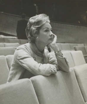 Black and white photo of a woman sitting in a theater with empty seats around her.